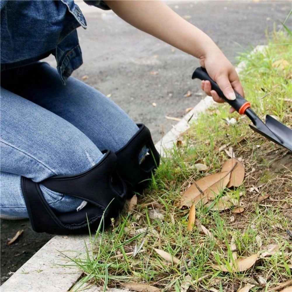A gardener wearing black knee pads while tending a garden border with a hand trowel